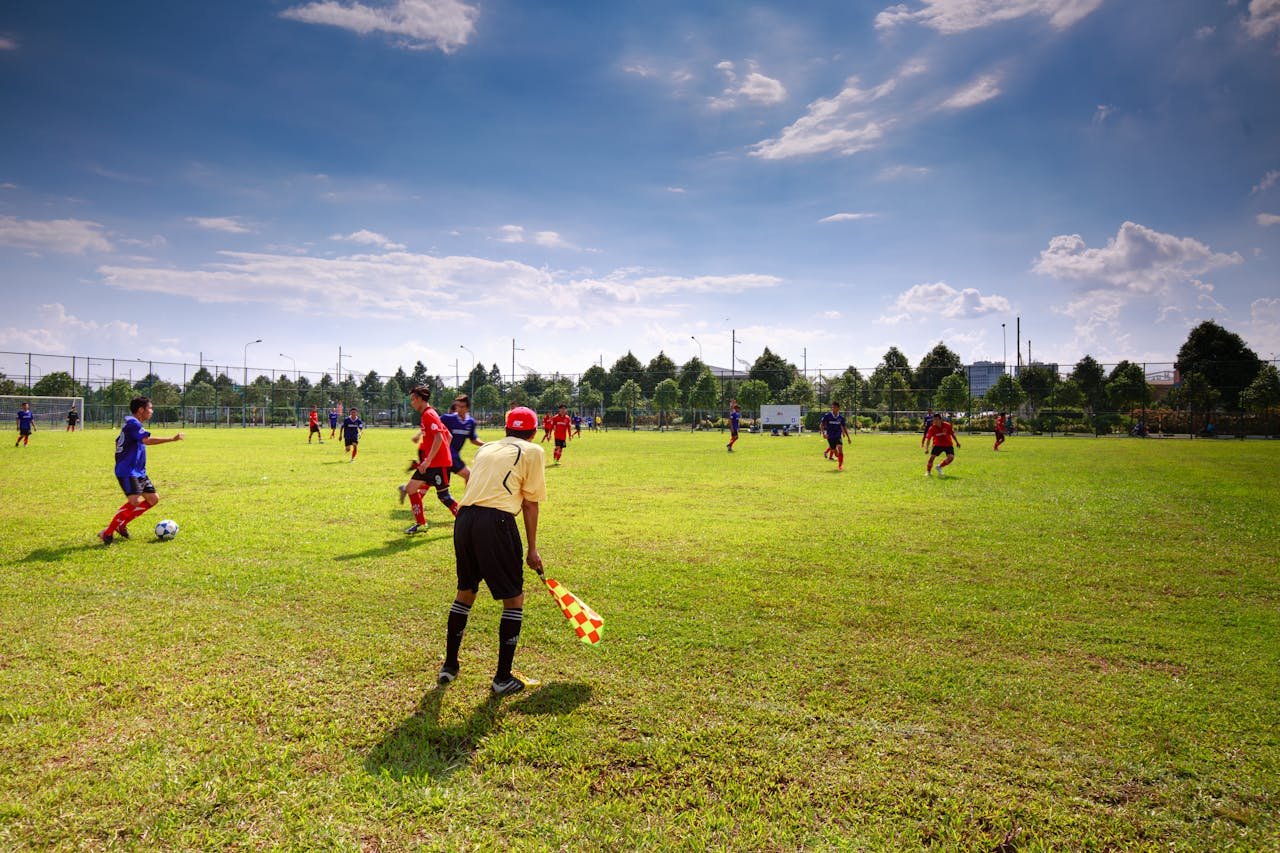 Youth soccer match in outdoor field with players, referee, and clear sky.